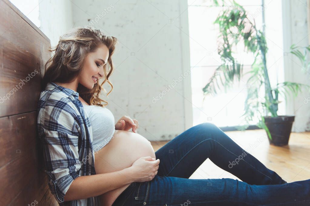 Happy pregnant woman sitting on the floor and touching her belly at home