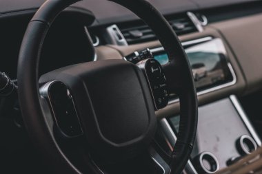 İçi koyu renkli lüks bir araba. Direksiyon, vites kolu ve gösterge paneli. Araç içi lüks. Direksiyon, hız göstergesi, görüntü, ışık panelleri