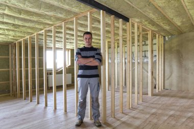 Genç yakışıklı Oluşturucu adam meşe döşeme ile büyük ferah ışık boş tavan odanın ortasında ayakta izole tavandan ve ahşap çerçeve gelecekteki duvarlar için. İnşaat ve tadilat kavramı.