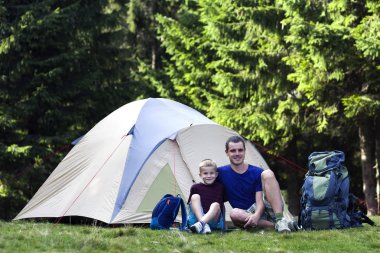 Tatil kamp. Baba ve oğlu Orman gezici ve açık hava etkinlikleri'da yürüyüş sonra dinlenme çadırı yakınındaki alarak. Mutlu aile ilişkileri ve sağlıklı yaşam tarzı.