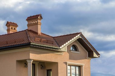 Kırmızı çatı shingled, iki yüksek bacalar, kar koruma düşük çit ve parlak mavi gökyüzü arka plan karşı Plastik pencere yeni büyük modern ev tepesinde. Profesyonelce yapılan inşaat iş kavramı.