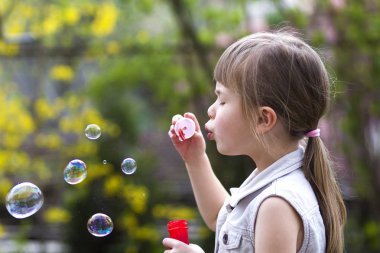 Profil renkli şeffaf sabun köpüğü açık havada üzerinde esen komik ciddi ifade ile oldukça küçük okul öncesi sarışın kızın yeşil yaz arka plan bulanık. Sevinç dikkatsiz çocukluk kavramının.