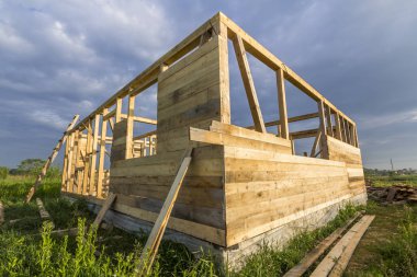 Mavi gökyüzü arka plan üzerindeki yeşil alanı inşaatı bitmemiş ekolojik ev. Çimento ve sakin alanda gelecekteki rahat yazlık pencere açıklıklar ahşap duvarlar siperler dolu.