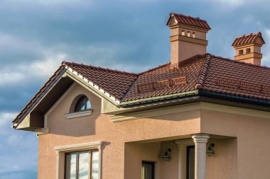 Kırmızı çatı shingled, iki yüksek bacalar, kar koruma düşük çit ve parlak mavi gökyüzü arka plan karşı Plastik pencere yeni büyük modern ev tepesinde. Profesyonelce yapılan inşaat iş kavramı.