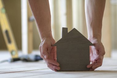 Kaslı erkek Close-up holding küçük kahverengi ahşap model ev araçları binanın arka plan bulanık eller. İnşaat, gayrimenkul ve rüya ev concept sahipliğini yatırımları.