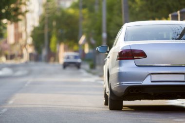 Yakın çekim geri görüntülemek yeni parlak pahalı gümüş arabanın hareketli şehir sokak üzerinde bulanık ağaçlar, arabalar ve binaların arka plan gün güneşli yaz boyunca. Rahat ulaşım ve modern hayat hız.