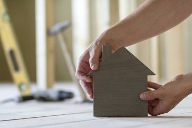 Kaslı erkek Close-up holding küçük kahverengi ahşap model ev araçları binanın arka plan bulanık eller. İnşaat, gayrimenkul ve rüya ev concept sahipliğini yatırımları.