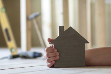 Kaslı erkek el küçük model ev tutarak Close-up araçları yapım aşamasında odasında binanın arka plan bulanık. Gayrimenkul ve rüya ev concept sahipliğini yatırımları.