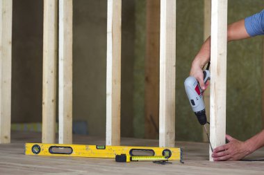 Yeniden yapılanma altında bitmemiş tavan odasında gelecekteki duvar için profesyonel araçlar ve ahşap çerçeve arka plan üzerinde tornavida ile işçi el Close-up. Yenileme ve iyileştirme kavramı.