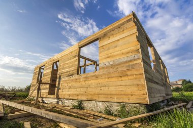 Mavi gökyüzü arka plan üzerindeki yeşil alanı inşaatı bitmemiş ekolojik ev. Çimento ve sakin alanda gelecekteki rahat yazlık pencere açıklıklar ahşap duvarlar siperler dolu.