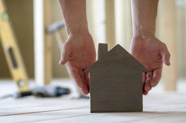 Kaslı erkek Close-up holding küçük kahverengi ahşap model ev araçları binanın arka plan bulanık eller. İnşaat, gayrimenkul ve rüya ev concept sahipliğini yatırımları.