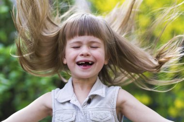 Güzel bir uzun saçlı sarışın okul öncesi kız utanarak kamera karşısına içine gülümseyerek kolsuz beyaz elbiseli portresi açık havada arka plan bulanık. Masum mutlu çocukluk kavramı.