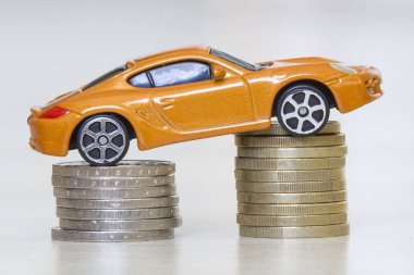 Metalik altın ve gümüş sikkelerin iki kazık üzerinde finansal refah, zenginlik, araç satış ve satınalma sembolü olarak yeni parlak parlak sarı lüks pahalı oyuncak spor araba yakın çekim fotoğraf.
