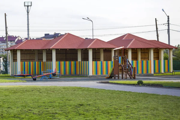 Bright new alcove with red tile roof and multicolored low fence on green lawn playground in kindergarten. Perfect place for happy games, recreation and entertainment, constructed with love and care.