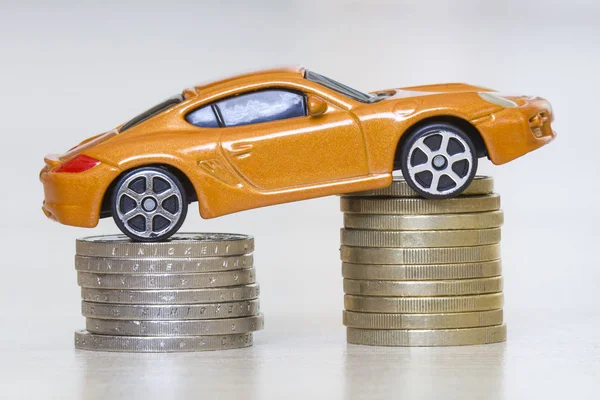 Metalik altın ve gümüş sikkelerin iki kazık üzerinde finansal refah, zenginlik, araç satış ve satınalma sembolü olarak yeni parlak parlak sarı lüks pahalı oyuncak spor araba yakın çekim fotoğraf.