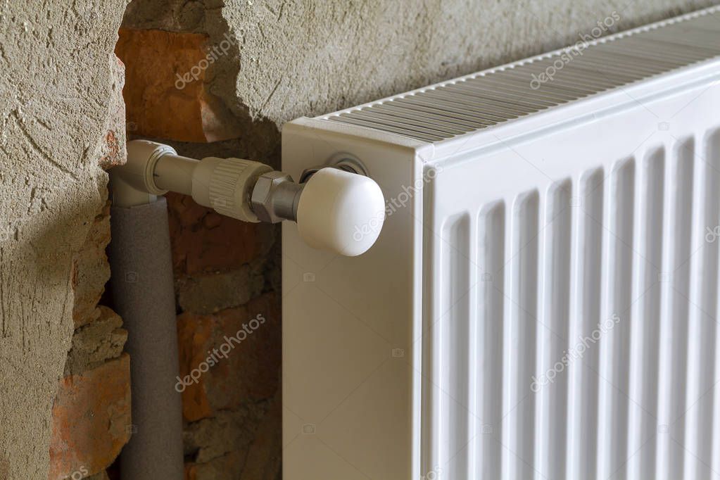 Close-up side view of isolated installed heating radiator on brick rough plastered wall in an empty room of a newly built apartment or house. Construction, maintenance, plumbing and repairing concept.