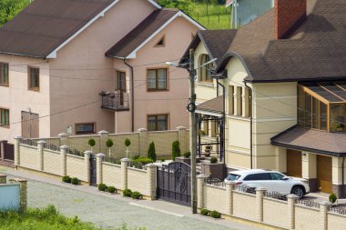 Sakin yerleşim bölgesinde yeni pahalı iki katlı evler tuğla çit ve kiremit çatılar ve döşeli bakımlı bahçesinde garaj kapısı önünde park edilmiş beyaz spor araba ile. Lüks ve refah kavramı.