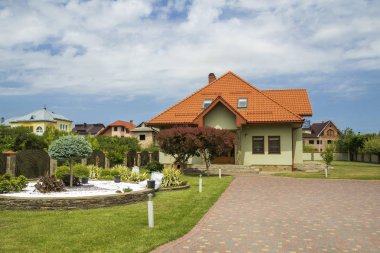 Shingle çatı, balkon, plastik tavan windows, taş döşeli Bahçe, yeşil çim ve parlak mavi gökyüzü arka plan üzerinde dekoratif çiçek açan ağaçlar ile yeni güzel tek katlı yazlık. Gayrimenkul mülkiyet kavramı.
