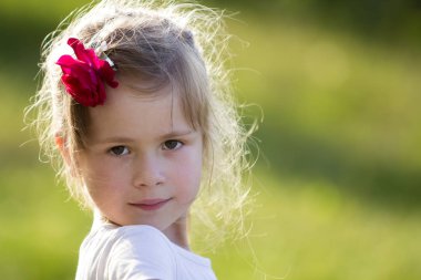 Portre güzel küçük okul öncesi sarışın kızın güzel gri gözleri ve kırmızı gül sersem kamera üzerinde gülümseyen saç parlak yeşil arka plan bulanık. Mutlu dikkatsiz çocukluk kavramı.