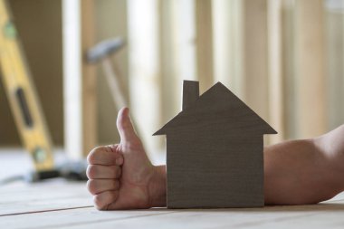 Küçük ahşap model müesseseden adamın el başparmak-up hareketi ile arka plan ve İnşaat aleti bulanık görüntüleri Close-up. Gayrimenkul ve rüya ev concept sahipliğini yatırımları.