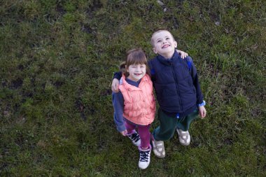 Yukarıdaki iki sevimli çocuk rahat kıyafetler, çocuk ve yeşil çimenlerin üzerinde duran, her diğer tarafı sarılma, yukarıya bakıp mutlu gülümseyen kız görüntüleyin. Mutlu çocukluk ve dostluk kavramı.