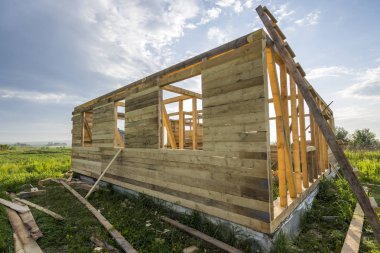 Mavi gökyüzü arka plan üzerindeki yeşil alanı inşaatı bitmemiş ekolojik ev. Çimento ve sakin alanda gelecekteki rahat yazlık pencere açıklıklar ahşap duvarlar siperler dolu.