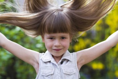 Güzel bir uzun saçlı sarışın okul öncesi kız utanarak kamera karşısına içine gülümseyerek kolsuz beyaz elbiseli portresi açık havada arka plan bulanık. Masum mutlu çocukluk kavramı.