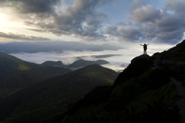 Geniş dağ panorama. Turist ile sırt çantası ile beyaz bulutlar kaplı vadi üzerinden kaldırdı elleriyle kayalık dağ yamacında küçük silüeti. Güzellik, Doğa, turizm ve seyahat kavramı