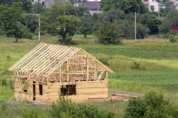 New wooden cottage of natural lumber materials with steep plank roof frame under construction in green neighborhood. Property, investment, professional building and reconstruction concept.