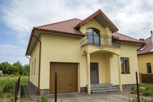 New yellow two-story residential cottage with shingle roof, front porch, plastic windows, high chimneys, balconies on blue sky background. Real estate property, architecture and prosperity concept.