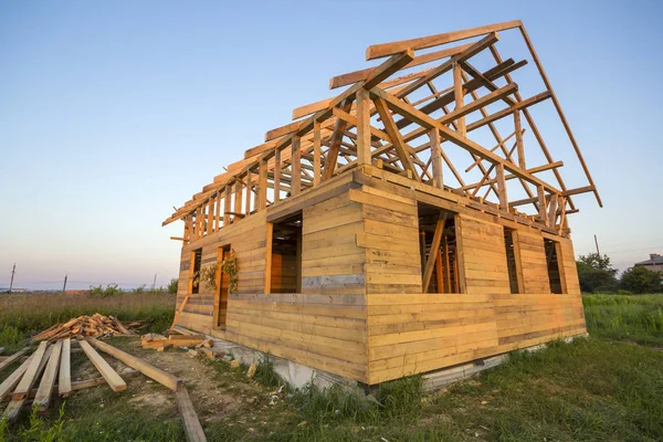 New cottage of natural ecological lumber materials under construction in green field. Wooden walls and steep roof frame. Property, investment, professional building and reconstruction concept.