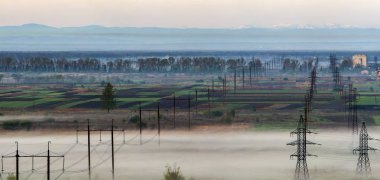Güzellikler ufuk bahar alanları ve ağaçların altında yoğun sabah sis uzak Karpat Dağları aralığı arka plan üzerinde uzanan uzun elektrik yüksek gerilim güç satır satır.