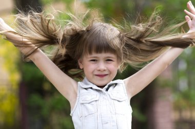 Rüzgar, komik dişsiz gülümseme ve arka plan bulanık yayılmış silah tarafından üflenir güzel uzun sarı saçlı kolsuz beyaz elbiseli küçük okul öncesi kız. Masum mutlu çocukluk kavramı.