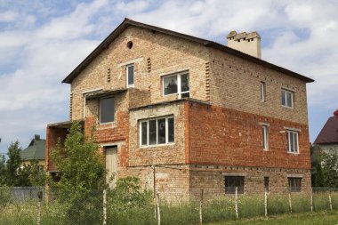 Yeni bitmiş tuğla ev bindik kapı girişi, birinci katta Plastik pencere ile tuğla ve yeşil çim çit karada çakıl yığınları arsa. İnşaat, gayrimenkul ve yatırım.