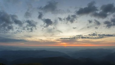 Fantastik gündoğumu veya günbatımı üzerinde yeşil dağ sırtı ile yoğun mavi sis kaplı. Parlak turuncu güneşin yumuşak bulutlu gökyüzü uzak ufukta yükselterek. Güzellik, Doğa, turizm ve seyahat kavramı.