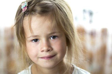 Gri gözleri ve utanarak kamera üzerinde gülümseyen dağınık sarı saçlı kız küçük sevimli genç ve güzel çocuk portresi gri arka plan bulanık. Güzellik, hayaller ve masum çocukluk kavramının.