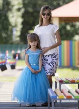 Genç Sarışın ince gülümseyen tam uzunlukta portresi güneş gözlüğü ve uzun mavi gece elbisesi anaokulu üzerinde küçük güzel kızım kız mutlu anne Bahçesi bulanık. Bakım ve kavram seviyorum.