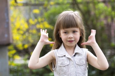 Güzel bir uzun saçlı sarışın okul öncesi kız utanarak kamera karşısına içine gülümseyerek kolsuz beyaz elbiseli portresi açık havada arka plan bulanık. Masum mutlu çocukluk kavramı.