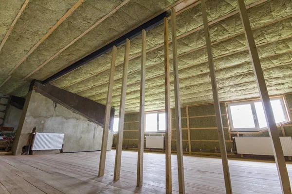 Construction and renovation of big light spacious empty room with oak floor, walls and ceiling insulated with rock wool, heating radiators under low attic windows and wooden frame for future walls.