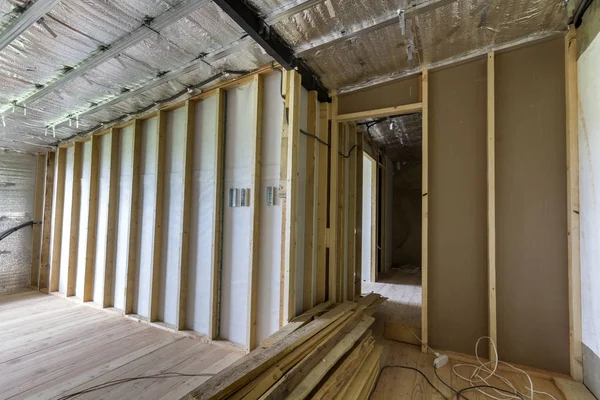 Room under construction and renovation with silver aluminum foil on walls and ceiling, oak floor and wooden timber frame for future partition wall. Professional reconstruction and insulation concept.