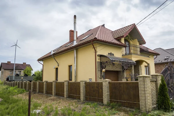 Yeni sarı iki katlı konut yazlık shingle çatı, ön sundurma, plastik pencere, yüksek bacalar, mavi gökyüzü arka plan üzerinde balkon ile. Gayrimenkul mülkiyet, mimari ve refah kavramı.