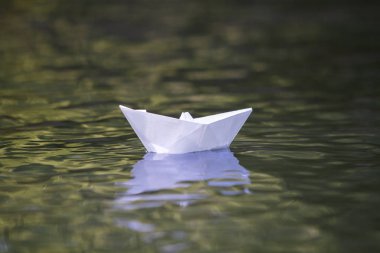 Basit küçük beyaz origami kağıt tekne sessizce sarı temiz nehir veya deniz su parlak yaz göğün altında yüzen Close-up. Özgürlük, düşler ve fantasies kavramı, boşaltmak arka plan.