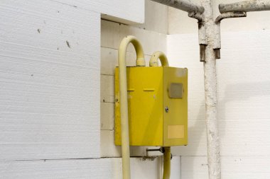 Ev duvar beyaz sert poliüretan styrophome sayfaları ile yalıtımlı köşesinde asılı borular bağlanma ile sarı gaz metre kutusunun yakın çekim. İnşaat, tadilat, enerji tasarrufu kavramı.