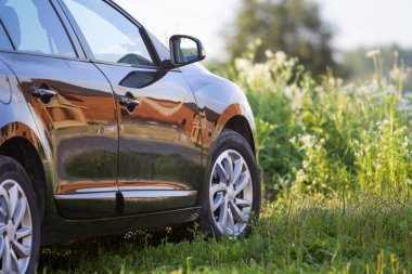 Modern yeni parlak boş siyah araba arkadan görünüm yol çimenli başgösteren alanındaki parlak yaz güneşli bulanık yeşil ağaçlar arka plan üzerinde dışarıda. Ulaştırma, kirlilik ve ekoloji kavramı.