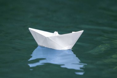 Basit küçük beyaz origami kağıt tekne sessizce parlak yaz göğün altında açık mavi nehir veya deniz suyu yüzen Close-up. Özgürlük, düşler ve fantasies kavramı, boşaltmak arka plan.