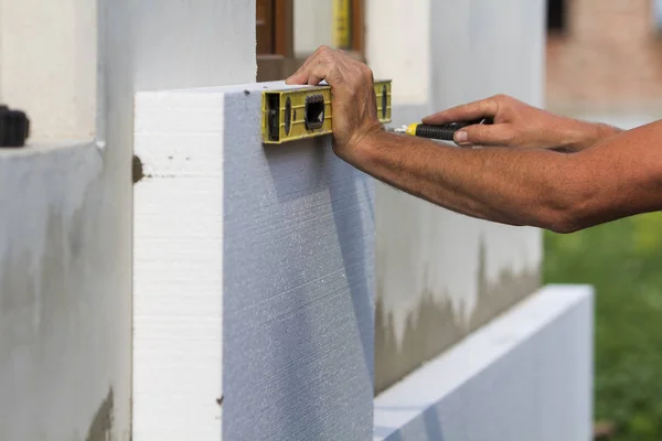 Worker hand with level and knife measuring and cutting white rigid polyurethane foam sheet on wall at newly installed plastic window. Modern technology, renovation, insulation concept.