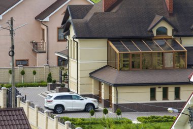 Sakin yerleşim bölgesinde yeni pahalı iki katlı evler tuğla çit ve kiremit çatılar ve döşeli bakımlı bahçesinde garaj kapısı önünde park edilmiş beyaz spor araba ile. Lüks ve refah kavramı.