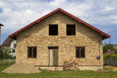Yeni bitmiş tuğla ev bindik kapı girişi, birinci katta Plastik pencere ile tuğla ve yeşil çim çit karada çakıl yığınları arsa. İnşaat, gayrimenkul ve yatırım.