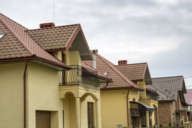 Yeni sarı iki katlı konut yazlık shingle çatı, ön sundurma, plastik pencere, yüksek bacalar, mavi gökyüzü arka plan üzerinde balkon ile. Gayrimenkul mülkiyet, mimari ve refah kavramı.