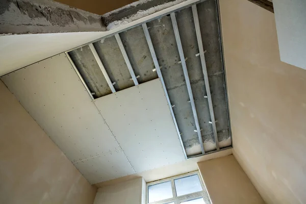 Angled view of light empty room under construction. Suspended ceiling and walls from drywall fixed to metal frame with screws. Renovation, insulation, comfort and do it yourself concept.